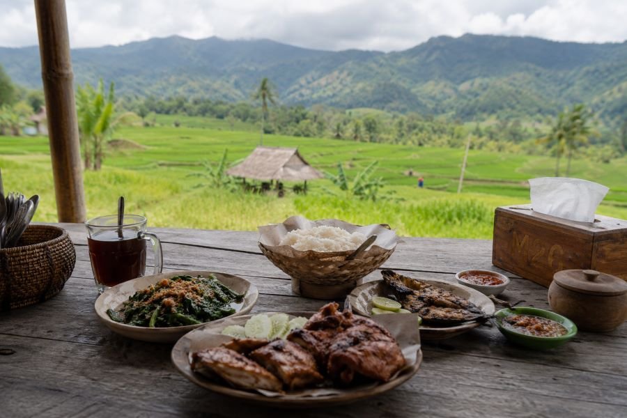 One thing people rarely explain properly about village food in Lombok is this: freshness changes everything.

Vegetables taste brighter. Chili feels sharper. Even plain rice somehow tastes… warmer? Hard to explain.

At a Tetebatu warung, meals are often cooked only after you order them. You wait a little longer, yes, but nobody really complains because the surroundings make waiting enjoyable. You stare at the rice fields. Maybe sip black coffee. Maybe hear distant roosters screaming for no reason.

Then the food arrives.

Plecing kangkung. Ayam taliwang. Fresh grilled fish. Sambal that wakes up your entire nervous system.

And somehow you keep eating even when you’re already full.